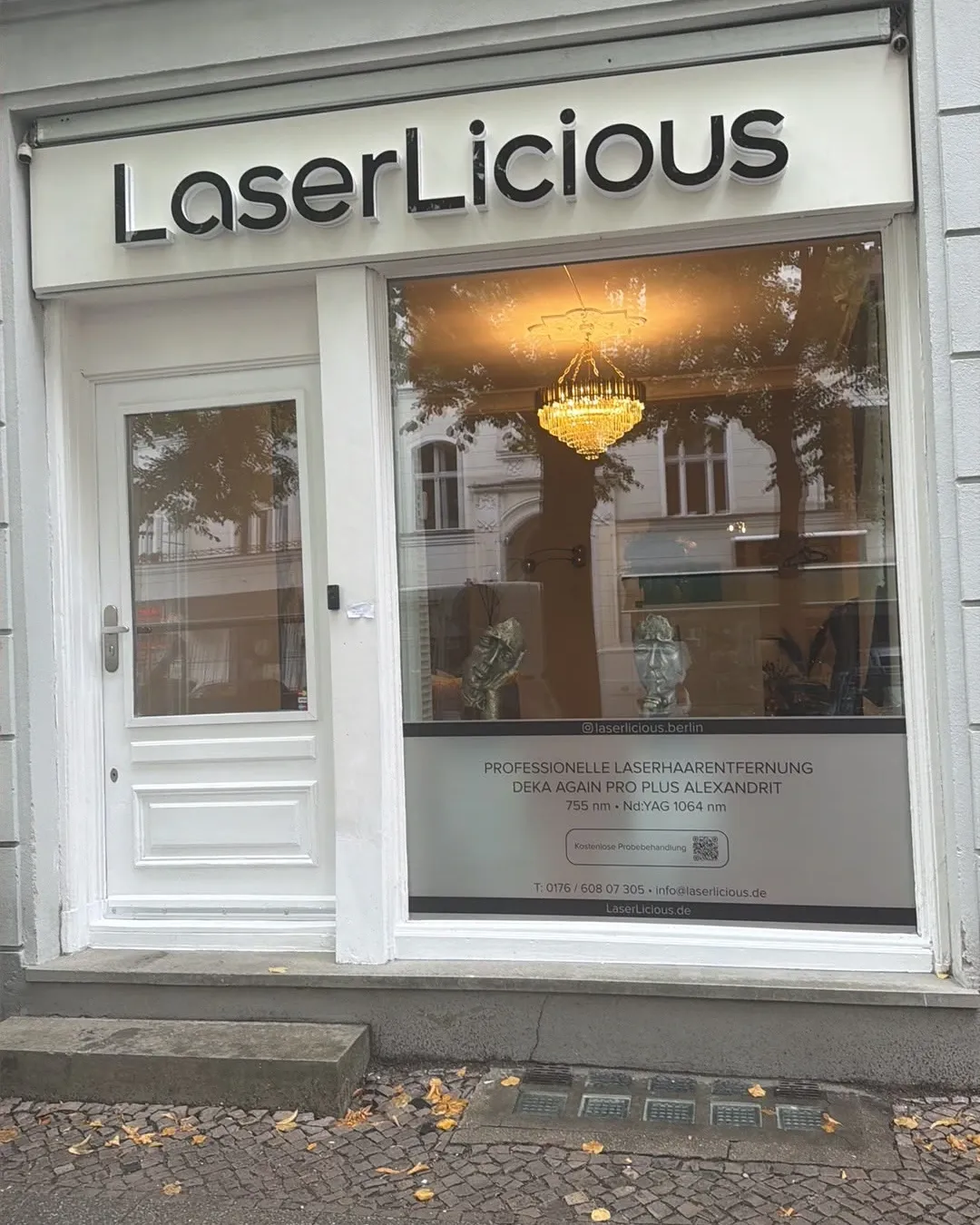 Eingang von LaserLicious in der Pariser Straße 7 in Berlin: weiße Tür, Schild über dem Schaufenster, Kronleuchter im Studio